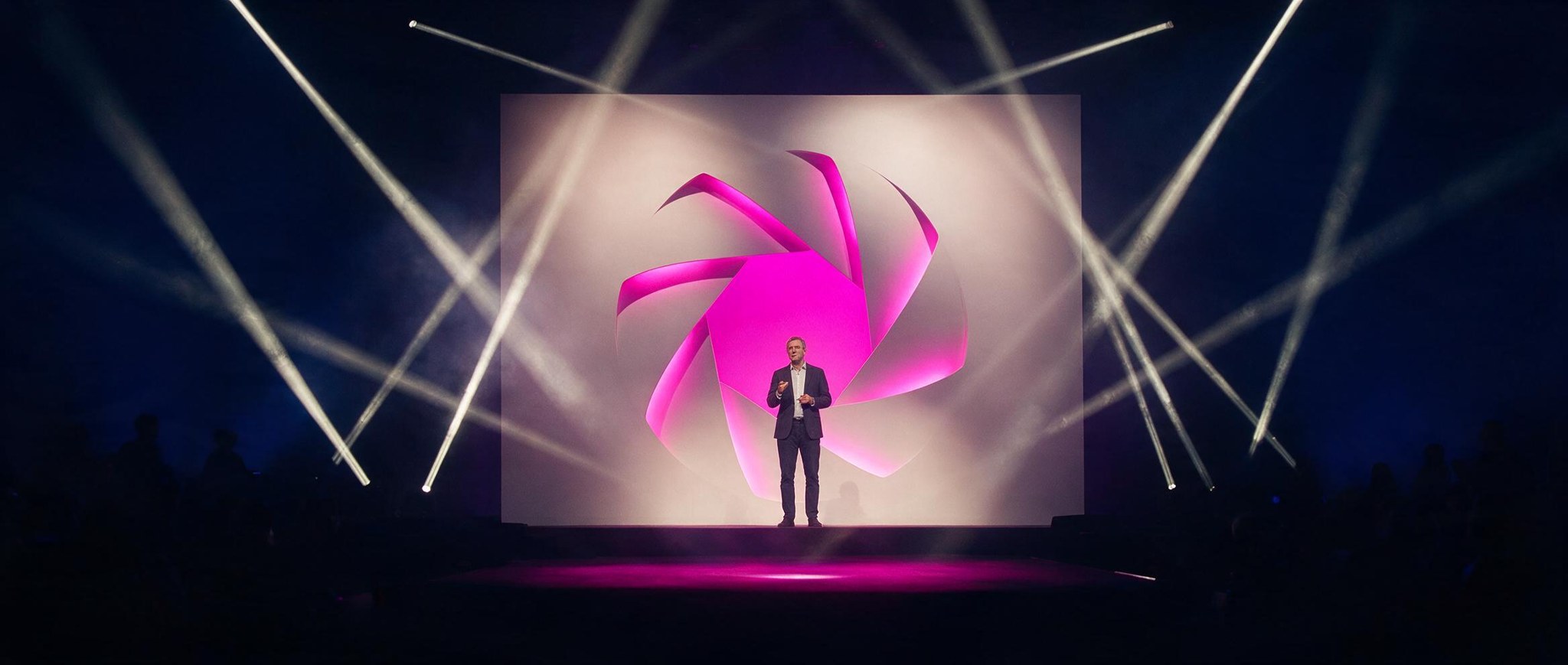 Cenografia do Palco Expo: diafragma vazado em magenta no telão, feixes de luz e o apresentador em silhueta